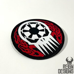 May include: A black and white embroidered patch with a skull and the Imperial symbol from Star Wars. The skull is surrounded by red flames.