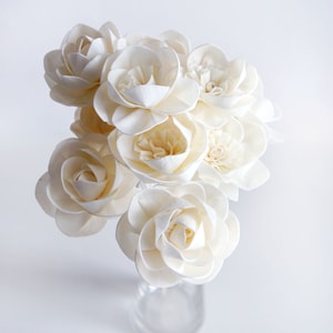 Peut inclure: Un bouquet de fleurs en bois de sola blanc dans un vase en verre transparent. Les fleurs sont disposées en grappe et ont une texture délicate et papier.