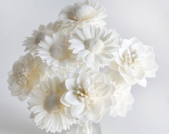 May include: A bouquet of white sola wood flowers in a clear glass vase. The flowers are arranged in a cluster and have a delicate, papery texture.