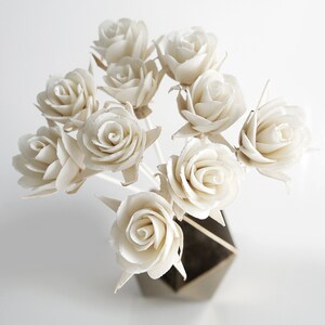 May include: A bouquet of white sola wood roses arranged in a vase. The roses are made of sola wood, which is a natural material that is lightweight and durable.