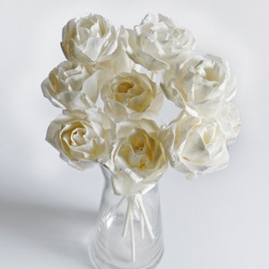 May include: A bouquet of white dried roses in a clear glass vase. The roses are arranged in a cluster and have a delicate, natural look.