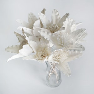 Peut inclure: Un bouquet de fleurs en papier blanc et crème dans un vase en verre transparent. Les fleurs ont une texture délicate et en couches et sont disposées dans un style lâche et naturel.
