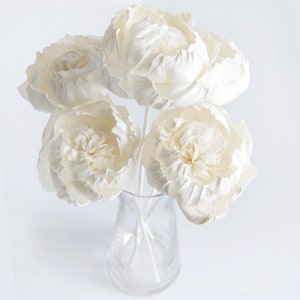 Op de afbeelding: Een boeket van vijf witte sola-houten bloemen in een heldere glazen vaas. De bloemen zijn in een tros gerangschikt en hebben een delicate, gekrulde textuur.