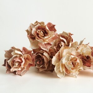May include: A bouquet of dried flowers in shades of brown and beige. The flowers are arranged in a loose, natural style, with some petals curled and others open wide. The flowers are delicate and have a rustic, vintage feel.