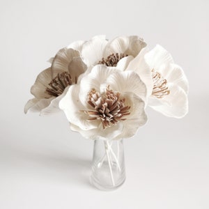 Op de afbeelding: Een boeket witte papieren bloemen met bruine centra in een heldere glazen vaas. De bloemen zijn op een eenvoudige en elegante manier gerangschikt, waardoor ze een mooie aanvulling zijn op elk interieur.