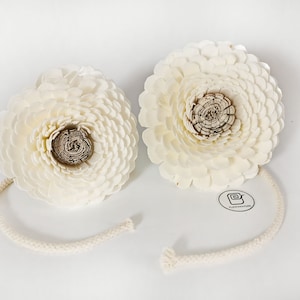 May include: Two white sola wood flower arrangements with a brown centre. Each flower is attached to a white cotton cord.