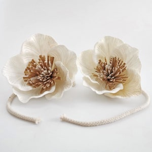 Op de afbeelding: Twee witte papieren bloemen met bruine centra, verbonden door een wit katoenen koord.