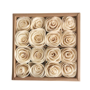 Peut inclure: Une boîte de 12 roses en bois de couleur crème disposées en grille. Les roses sont en bois et ont un aspect naturel et rustique.