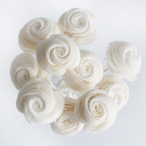 May include: A bouquet of white paper roses, arranged in a circular pattern. The roses are made of thin, layered paper and have a delicate, vintage aesthetic.