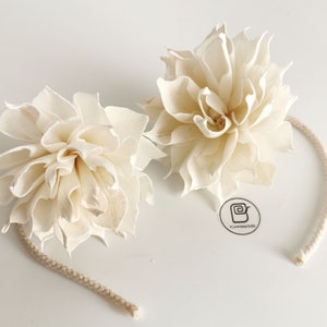 Op de afbeelding: Twee witte sola-houten bloempomanders met een wit touwtje. De bloemen zijn in een ronde vorm gerangschikt en hebben een delicate, gelaagde textuur. De bloemen zijn aan elkaar gebonden met een wit touwtje.