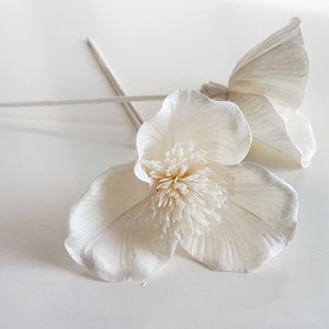 Op de afbeelding: Twee witte papieren bloemen met een getextureerd midden. De bloemen zijn bevestigd aan een witte stengel.