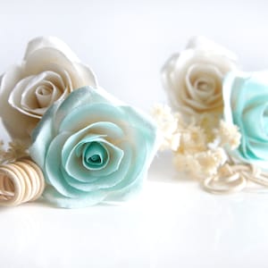 May include: A bouquet of artificial flowers with two white roses and one light blue rose. The bouquet is accented with dried white flowers and a wooden ring.