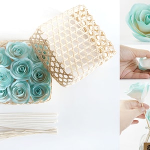 May include: A set of 10 light blue paper roses in a woven basket with white sticks for a diffuser. The roses are arranged in a circular pattern and have a white center.