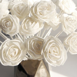 Peut inclure: Un bouquet de bâtonnets diffuseurs en bois blanc en forme de rose dans un vase doré. Les roses sont disposées en cercle et sont toutes orientées dans la même direction.
