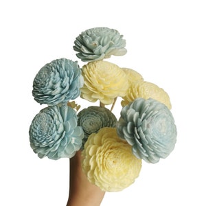 Peut inclure: Un bouquet de fleurs en bois de sola dans des tons de bleu et de jaune. Les fleurs sont disposées dans une main, les tiges pointant vers le haut.