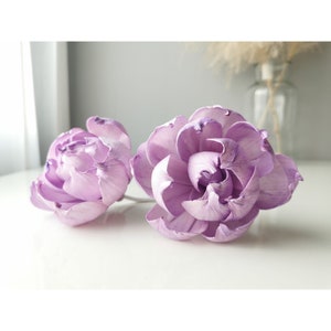 Op de afbeelding: Twee lavendelkleurige sola-houten bloemen met een delicate, gekrulde textuur. De bloemen zijn op een wit oppervlak gerangschikt.