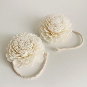 Op de afbeelding: Twee witte sola-houten bloemdiffusers met een wit touwtje aan elk. De bloemen zijn rond en hebben een gelaagd ontwerp.