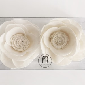 May include: Two white fabric rose-shaped air fresheners in a clear plastic box. The box has a white label with the text "PLAYAWANATURE" and a stylized image of a rolled-up fabric.