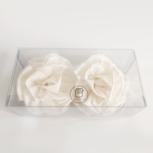 May include: Two white fabric rose-shaped flowers in a clear plastic box with the text "Playwana Sure" in a circle.