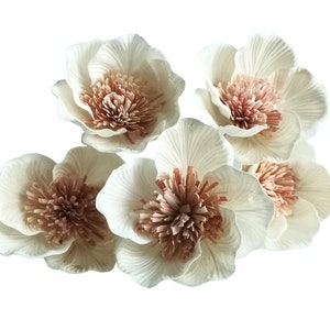 May include: Five white paper flowers with pink centres. The flowers are arranged in a cluster and have a delicate, layered appearance.