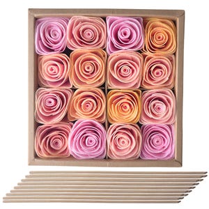 May include: A square cardboard box containing sixteen artificial roses arranged in a four-by-four grid. The roses feature gradient shades of pink, peach, and orange. Below the box are several thin, light brown wooden sticks laid out horizontally.