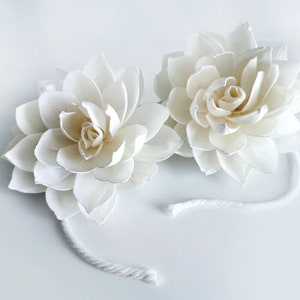 Op de afbeelding: Twee witte sola-houten bloemkoppen met een wit touwtje eraan.