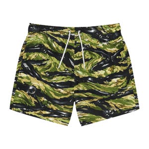 Könnte beinhalten: Grün, schwarz und beige Camouflage-Badeshorts mit weißem Kordelzug. Die Shorts haben ein wellenförmiges Muster und einen schwarzen, elastischen Bund. Hergestellt aus leichtem Material.