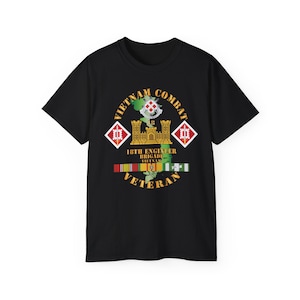 Puede incluir: Camiseta negra con un diseño circular que dice "VIETNAM COMBAT VETERAN". El diseño incluye un mapa, un castillo y las palabras "18TH ENGINEER BRIGADE VIETNAM". También se incluyen cintas y formas de diamante.