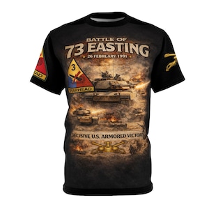 May include: Black t-shirt featuring a graphic of tanks in a battle scene with the text "BATTLE OF 73 EASTING 26 FEBRUARY 1991" and "DECISIVE U.S. ARMORED VICTORY". The shirt also includes a unit patch.