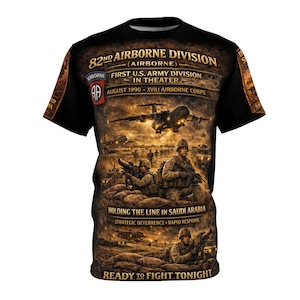 Puede incluir: Camiseta negra con un gráfico detallado que representa soldados, aviones y texto. El texto incluye "82nd Airborne Division", "First U.S. Army Division in Theater" y "Holding the Line in Saudi Arabia". El diseño tiene un tema militar.