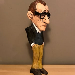 Op de afbeelding: Een handgemaakt papieren mach&eacute; beeldje van een man in een zwart pak, een blauwe trui en een bruine broek. Hij draagt een zwarte bril en heeft een grote neus.