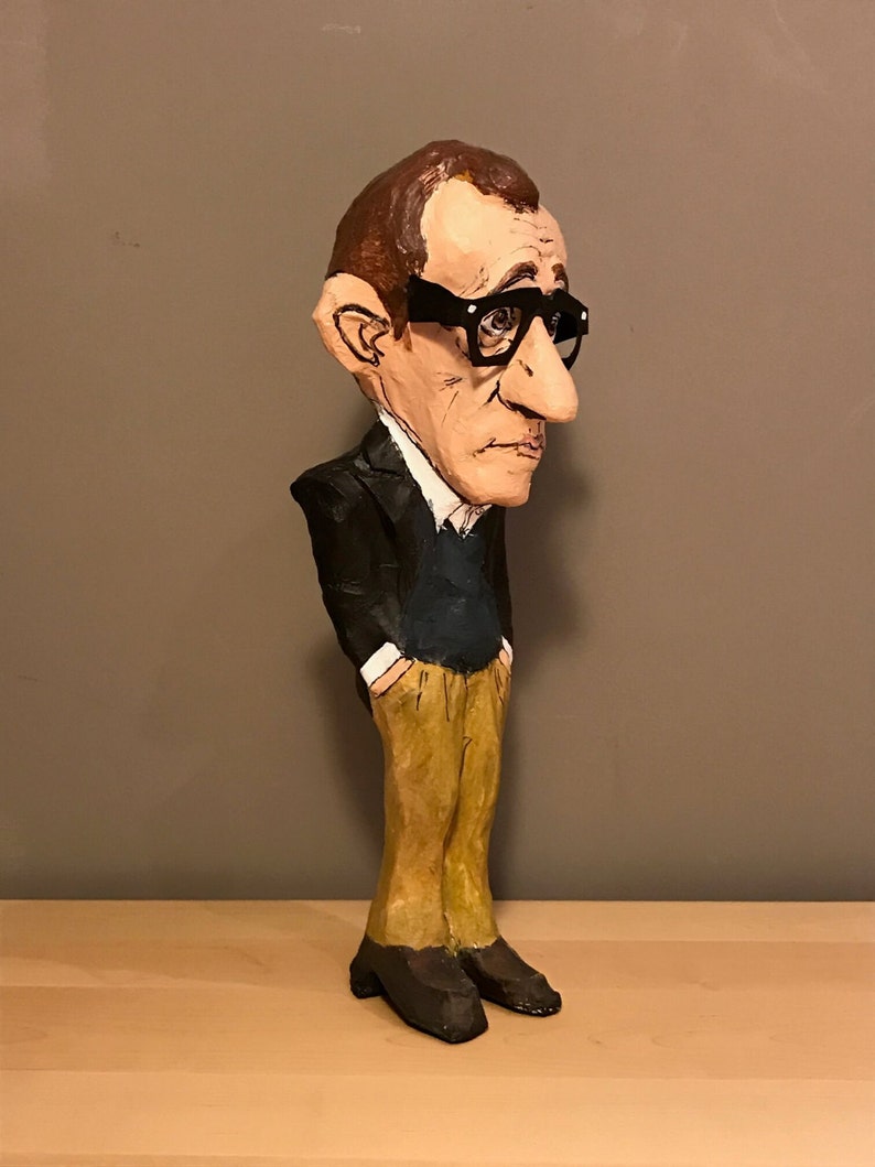 Op de afbeelding: Een handgemaakt papieren mach&eacute; beeldje van een man in een zwart pak, een blauwe trui en een bruine broek. Hij draagt een zwarte bril en heeft een grote neus.