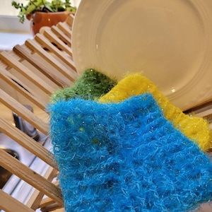 May include: Three colorful dishcloths in a wooden dish rack. The dishcloths are made of a soft, fluffy material and are blue, green, and yellow.