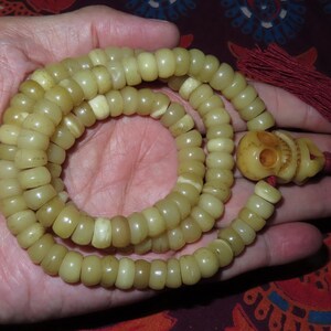 May include: A string of light yellow beads with a carved bone skull charm and a red tassel.