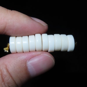 May include: A strand of white beads with a gold thread running through them. The beads are round and smooth, and they are strung together in a tight, even pattern.