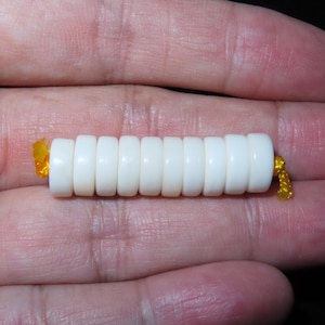 May include: A white bone bead bracelet with a yellow string tie. The bracelet is made of 10 round beads.