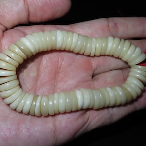 May include: A white shell bead bracelet with a red string closure. The bracelet is made of many small, round beads.