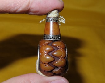 May include: A small, brown, carved amber-coloured object with a textured, petal-like surface. It features a smooth, tapered neck topped with a silver-coloured metal band decorated with small circular indentations and a light-coloured cord.