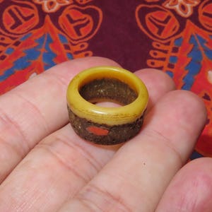 May include: A handcrafted ring with a yellow top and a dark brown base. The ring features a small red accent. This unique ring is a piece of jewelry.
