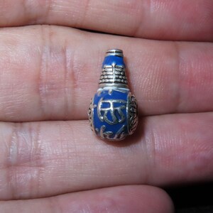 Peut inclure: Un petit charme bleu et argent avec des motifs complexes. Le charme est en forme de bouteille et a un bouchon argenté.