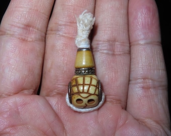May include: A small, white bone bead with a carved skull design and silver accents. The bead is attached to a white string.