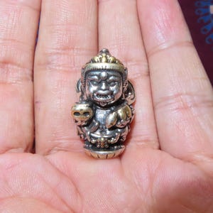 Könnte beinhalten: Kleine, detaillierte Silberfigur einer Gottheit, gehalten in einer Hand. Die Figur hat einen strengen Ausdruck, mit goldenen Akzenten auf der Krone und anderen Bereichen. Es ist ein religiöses oder spirituelles Objekt.
