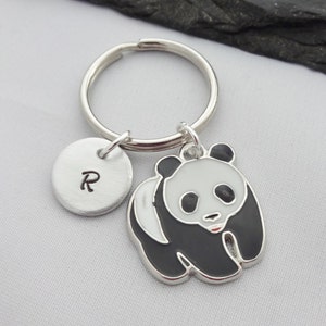 May include: A silver keychain with a black and white panda charm and a silver disc charm with the letter 'R' engraved on it.
