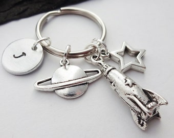 May include: Silver keychain with a rocket, a planet, a star, and a round charm with the letter J.