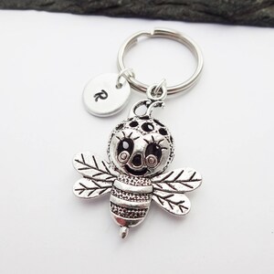May include: Silver bee keyring with a charm that says "R" on a silver key ring.