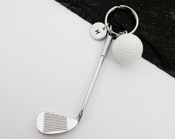 Könnte beinhalten: Silberner Golfschläger-Schlüsselanhänger mit einem weißen Golfball und einem silbernen Anhänger mit dem Buchstaben H.