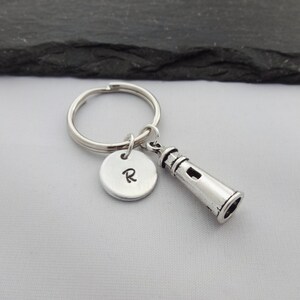 Puede incluir: Llavero de plata con un dije de faro y un dije redondo con la letra R grabada.