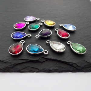 Puede incluir: Surtido de dijes de cristal en forma de l&aacute;grima con lazos de metal plateados. Los dijes son de varios colores, incluyendo rojo, verde, azul, morado y transparente.