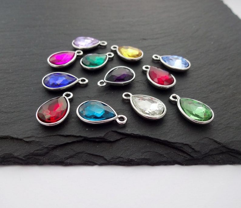 Puede incluir: Surtido de dijes de cristal en forma de l&aacute;grima con lazos de metal plateados. Los dijes son de varios colores, incluyendo rojo, verde, azul, morado y transparente.