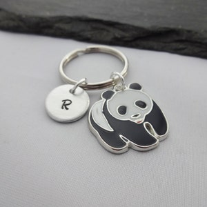 May include: A silver keychain with a black and white panda charm and a silver charm with the letter R engraved on it.